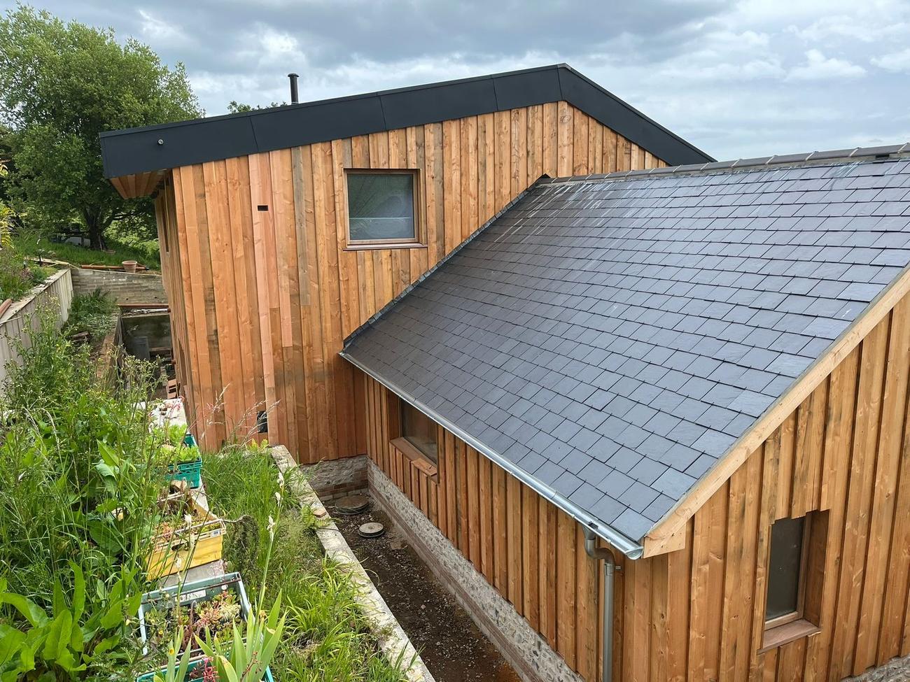 Larch cladding meeting a natural slate roof on a Dorset new build