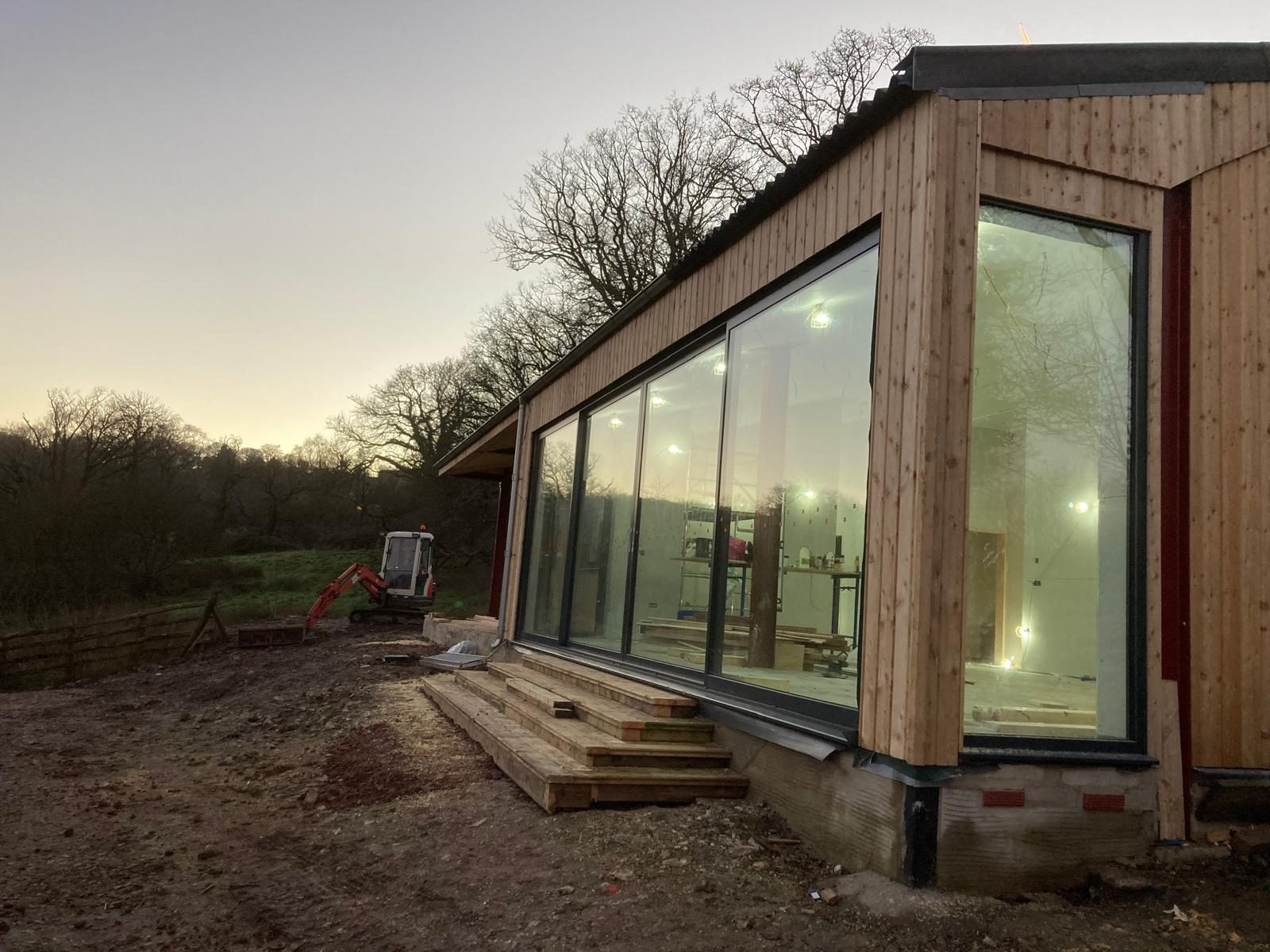 Larch-clad building with full-height corner glazing at dusk, West Dorset