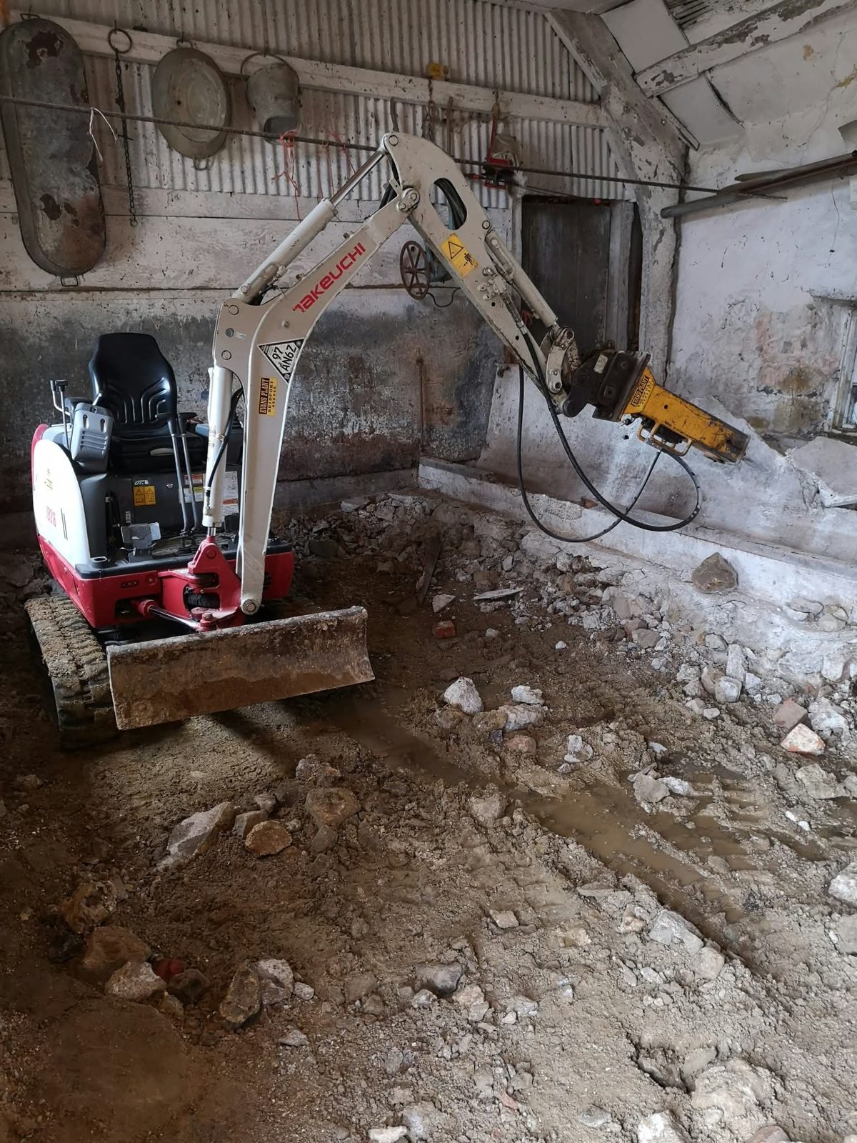Mini digger digging out the floor inside a stone barn